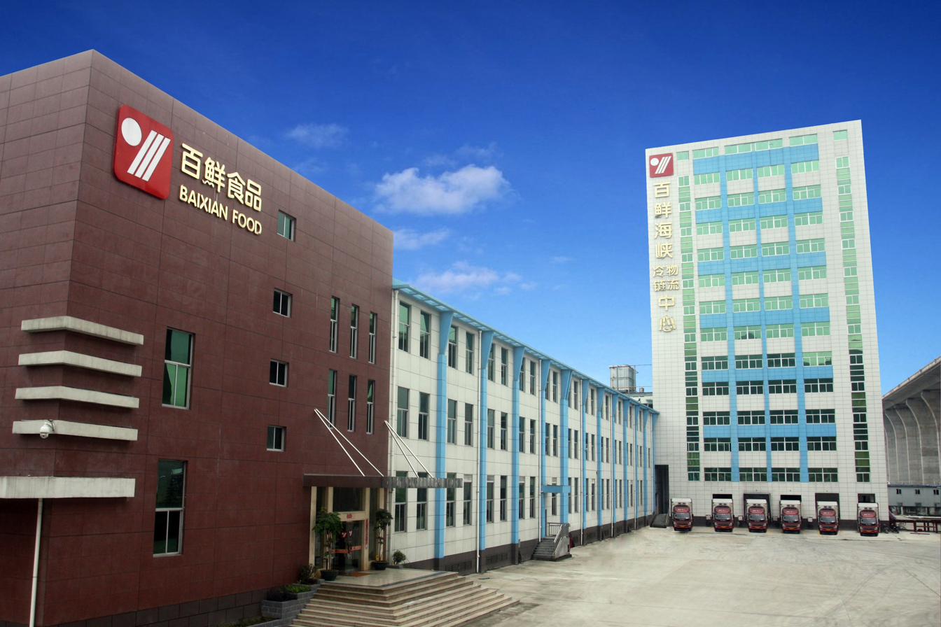 Exterior of the Baixian Strait Logistics Center in Mawei, Fuzhou — Baixian Food building on the left, cold logistics center tower on the right, refrigerated trucks loading at the dock.