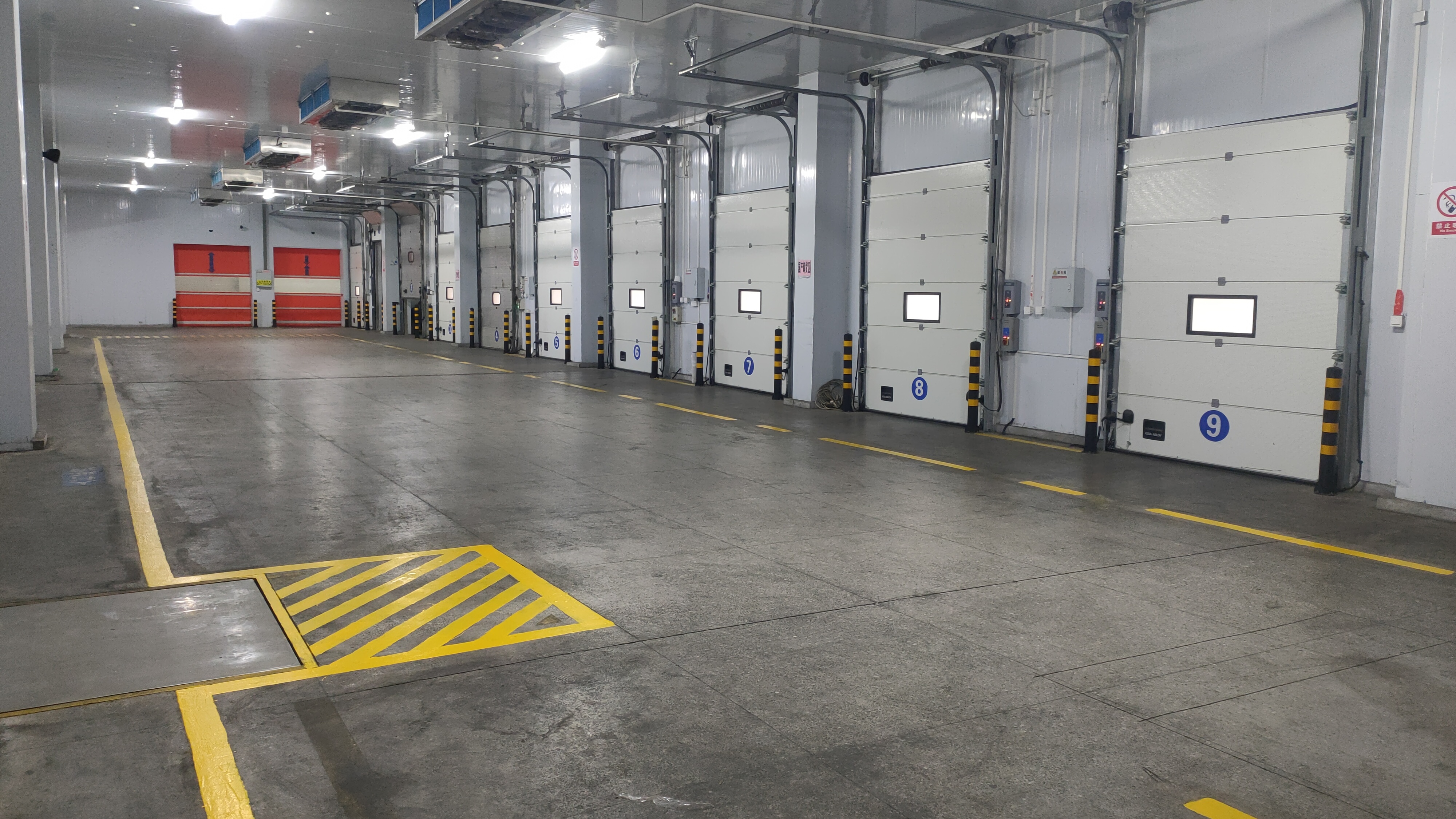 Loading dock interior at the Baixian Strait Logistics Center — numbered overhead bay doors, marked floor lanes, operational cold-storage scale visible.